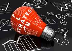 Una bombilla roja que tiene escrito 'Plan Estrategy' sobre una pizarra con gráficos