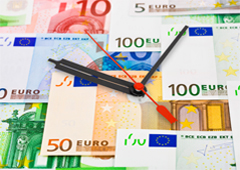 Un reloj sobre billetes y monedas de euro.