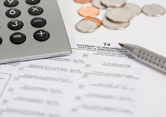 Una calculadora, un boli, y unas monedas sobre unos papeles